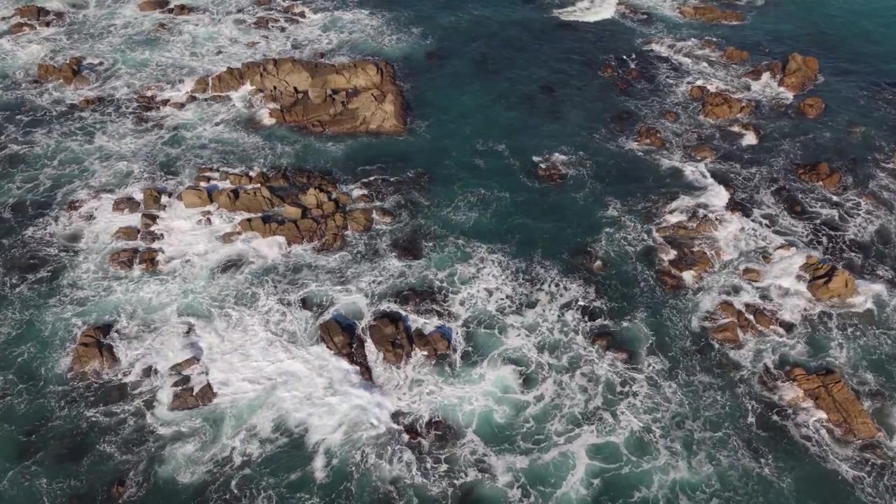 Riprese aeree con drone di affioramenti rocciosi sotto il sole del tardo pomeriggio, con onde che si infrangono sugli scogli in un mare blu cristallino e vista sul fondale marino.