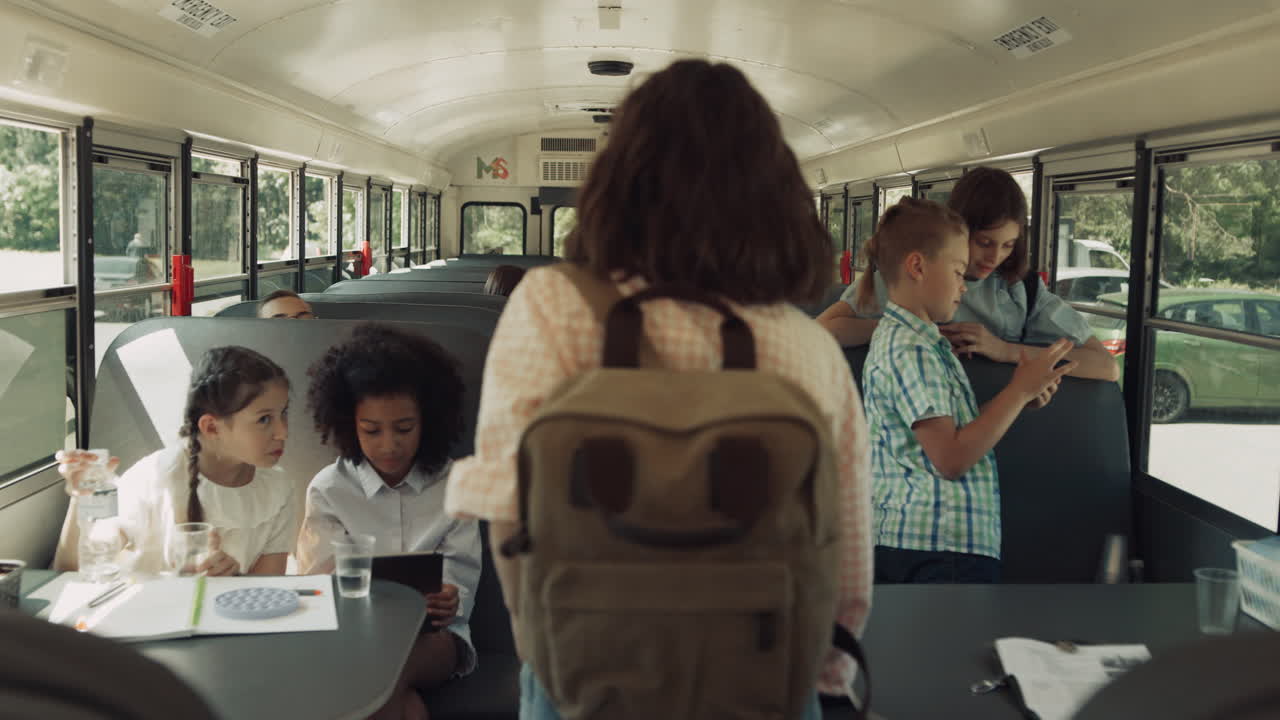 Teenageelever stiger på skolebussen. Forskellige børn bruger gadgets i køretøjet.