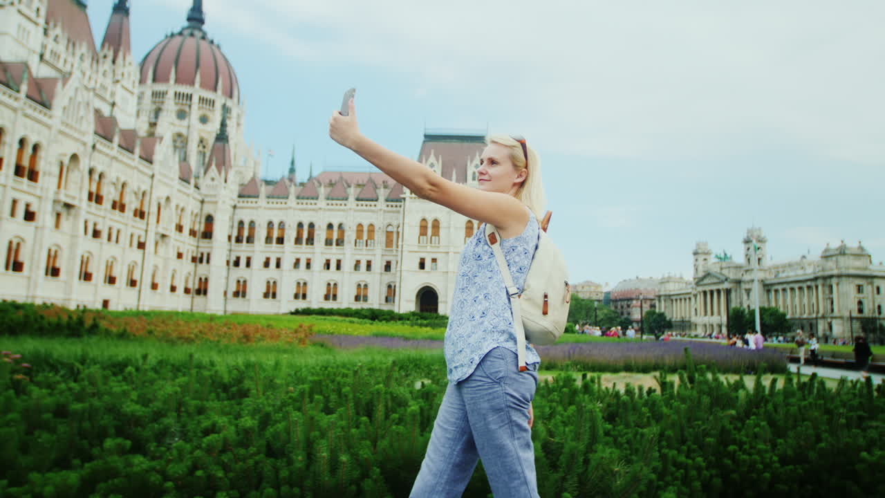 젊은 여성은 부다페스트 1에서 헝가리 의회를 배경으로 자신의 사진을 찍습니다.