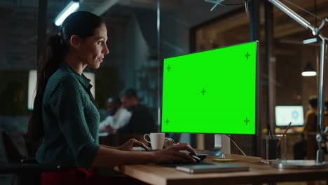 especialista multiétnico de mediana edad trabajando en una computadora de escritorio con pantalla verde en una oficina creativa ocupada. hermosa gerente femenina diversa en blusa verde con puntos de polca.