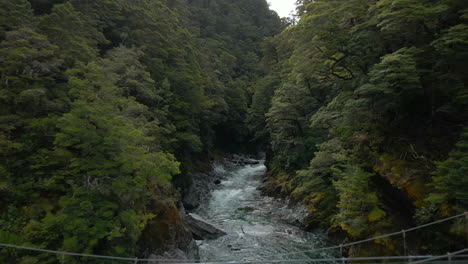 Aerial-view-of-metal-bridge-crossing-deep-narrow-river-in-Blue-Pools-in-New-Zealand