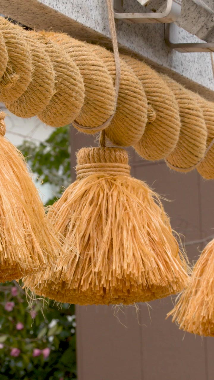 Primo piano di una spessa corda shimenawa con nappe pendenti da un torii di pietra.