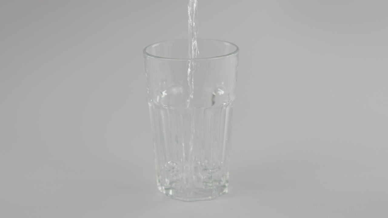 slowmotion trancado ainda água derramando em vidro transparente na frente de fundo neutro