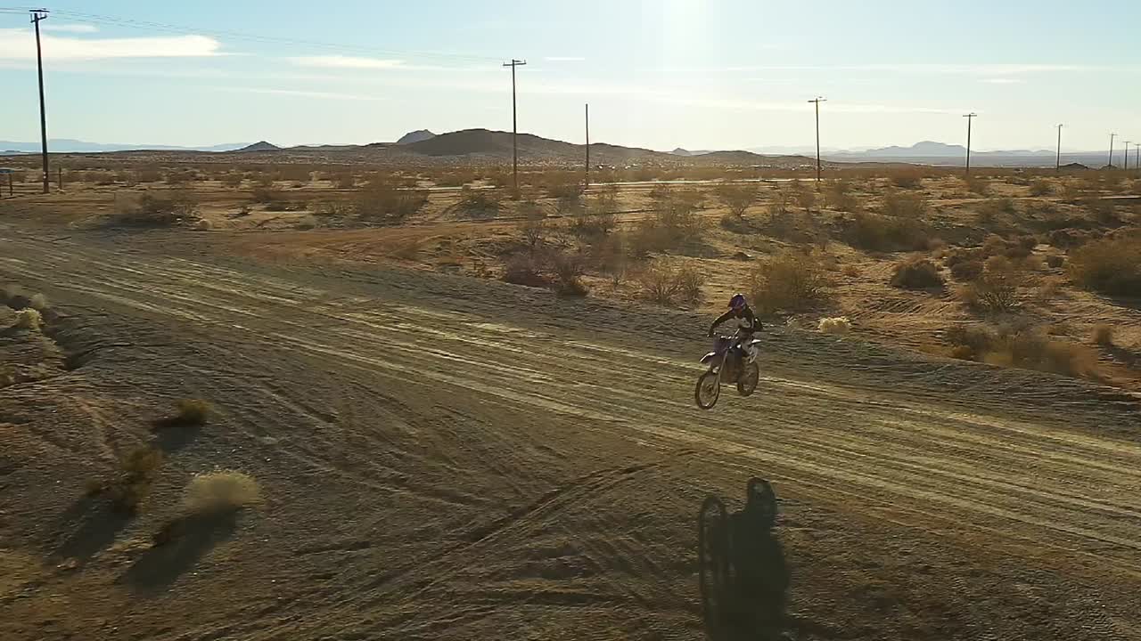 motociclista saltando a través de una carretera en el desierto de mojave en cámara lenta - vista aérea