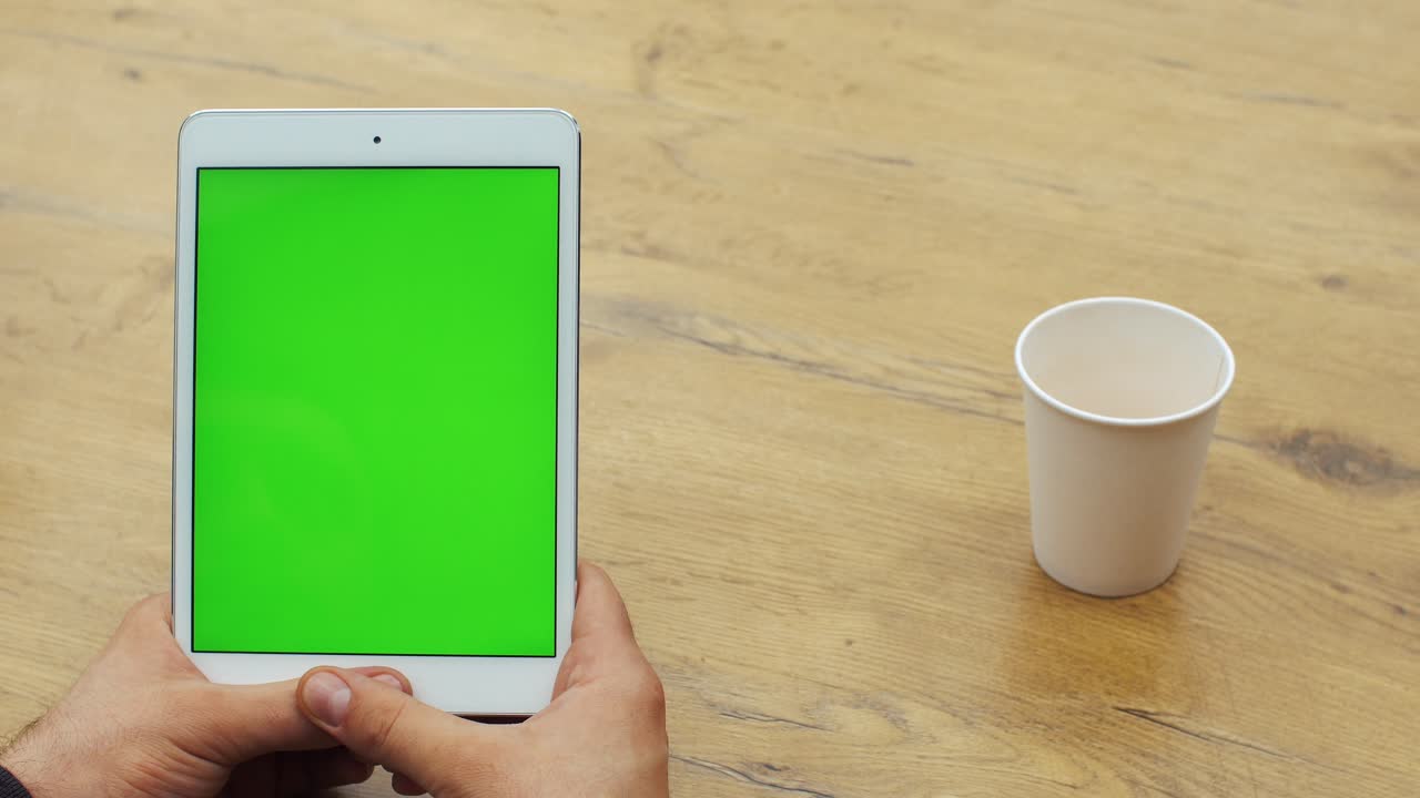 Tablet con schermo verde e bicchiere di carta su tavolo di legno