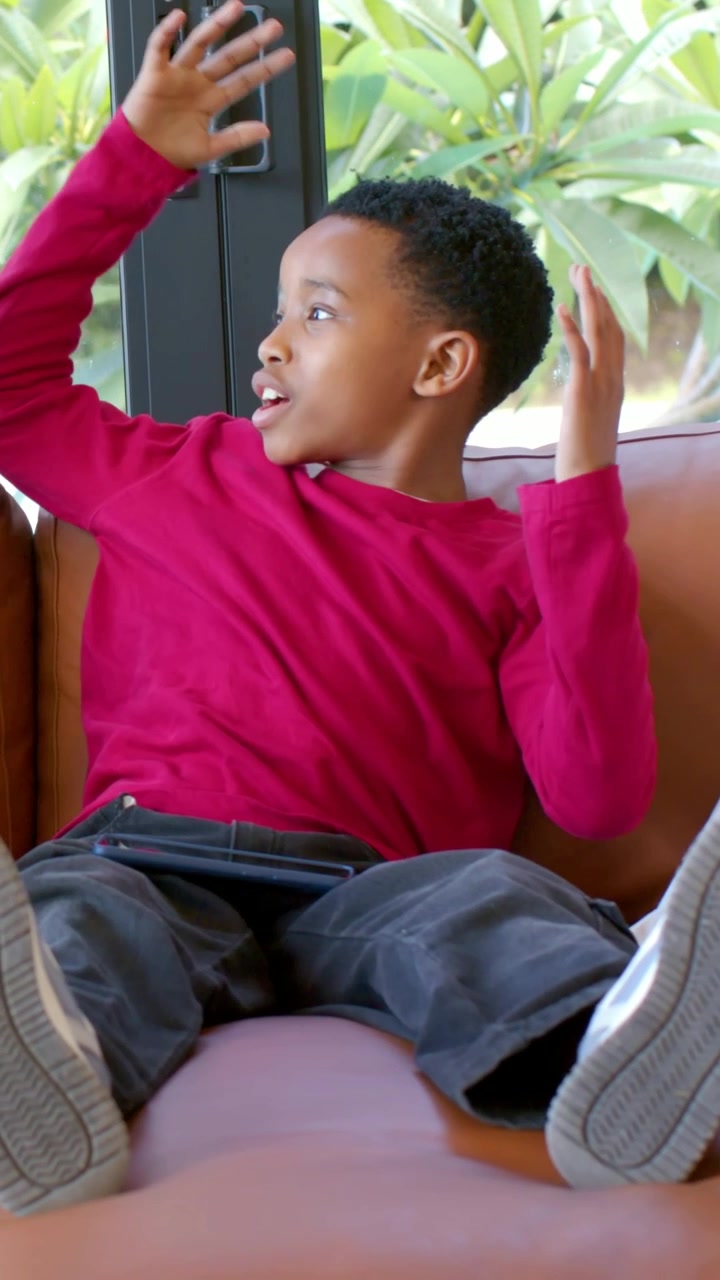 Vertical video: Reacting child turning and gesturing to offscreen event on brown couch in red shirt