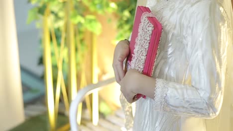 young pious beautiful muslimah woman wearing white veil - holding and hugging the holy book of quran as islamic religion basic universal knowledge source