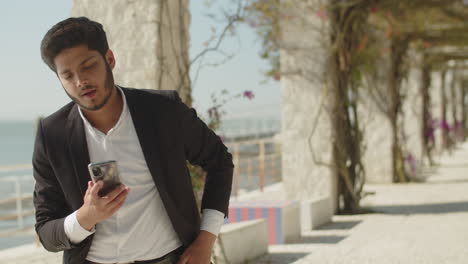 Dark-haired-muslim-man-in-suit-texting-message-outside.