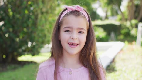 video portrait of happy caucasian girl with long hair and missing tooth smiling to camera in garden