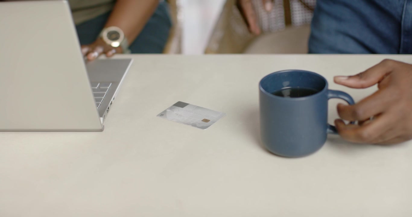 Right hand is bringing blue ceramic mug onto light tabletop, placing it near card for reach