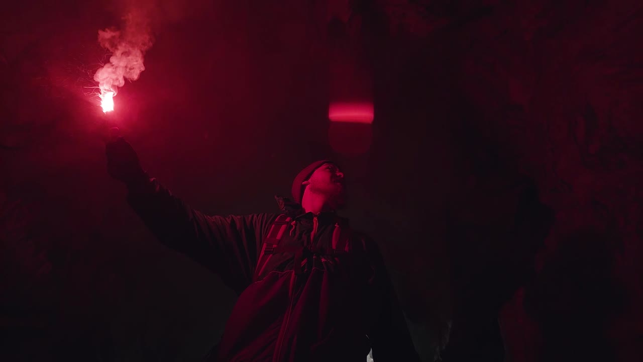 persona sosteniendo una llamarada roja en una cueva por la noche
