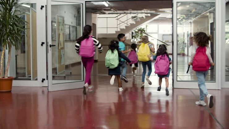 Vista trasera de un grupo feliz y multiétnico de escolares con mochilas coloridas corriendo por el pasillo de la escuela.