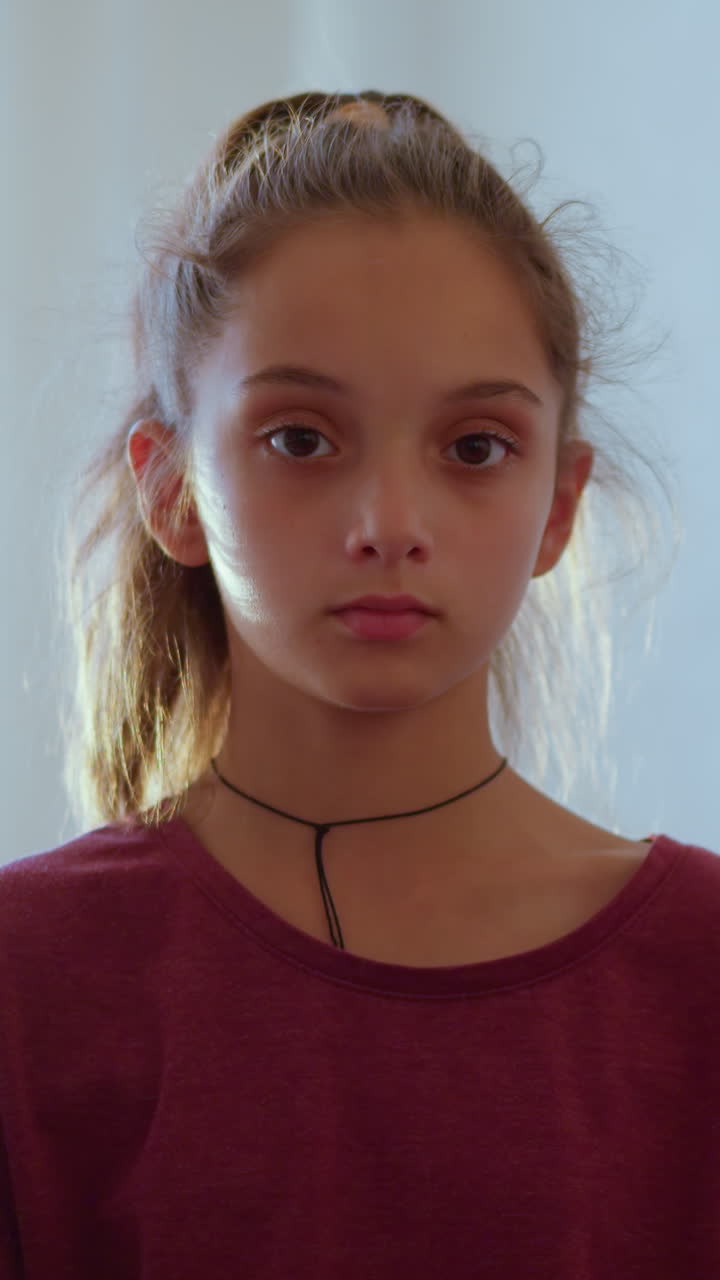 Thoughtful girl with ponytail in maroon shirt stands holding thermometer while observing something with serious focused expression showing concern awareness