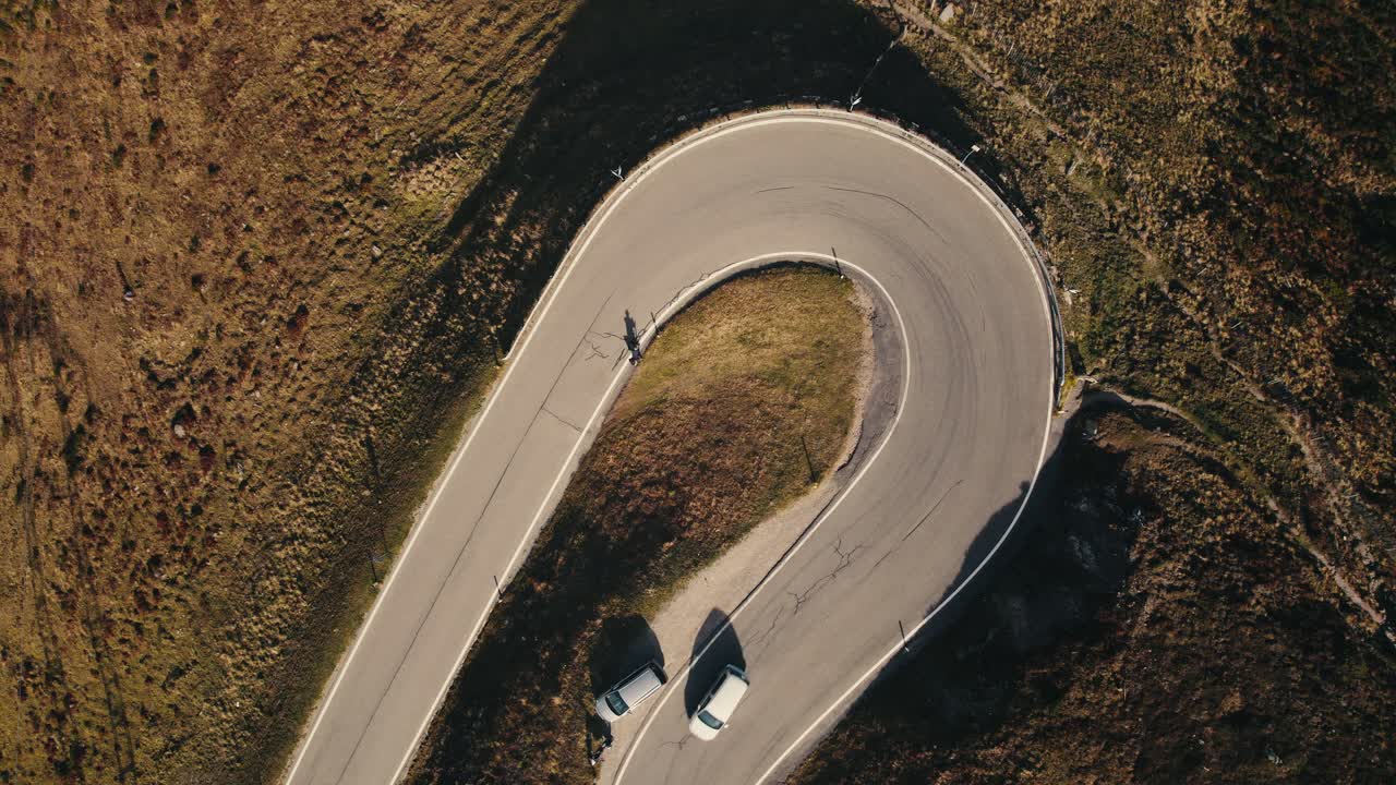 Luftfoto af en snoet vej med en cyklist og biler, omgivet af barskt terræn