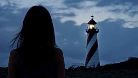 woman silhouetted against lighthouse at sunset