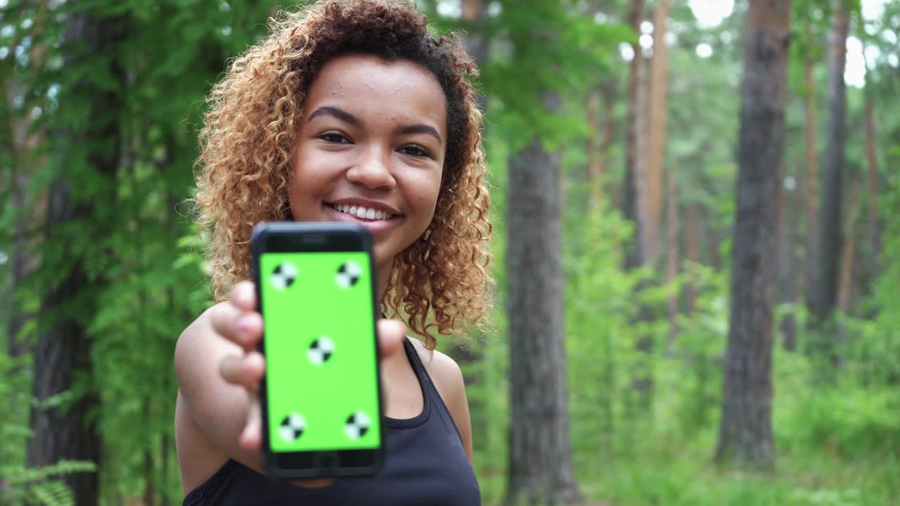 joven negra usando su teléfono inteligente después de correr y muestra la pantalla verde a la cámara
