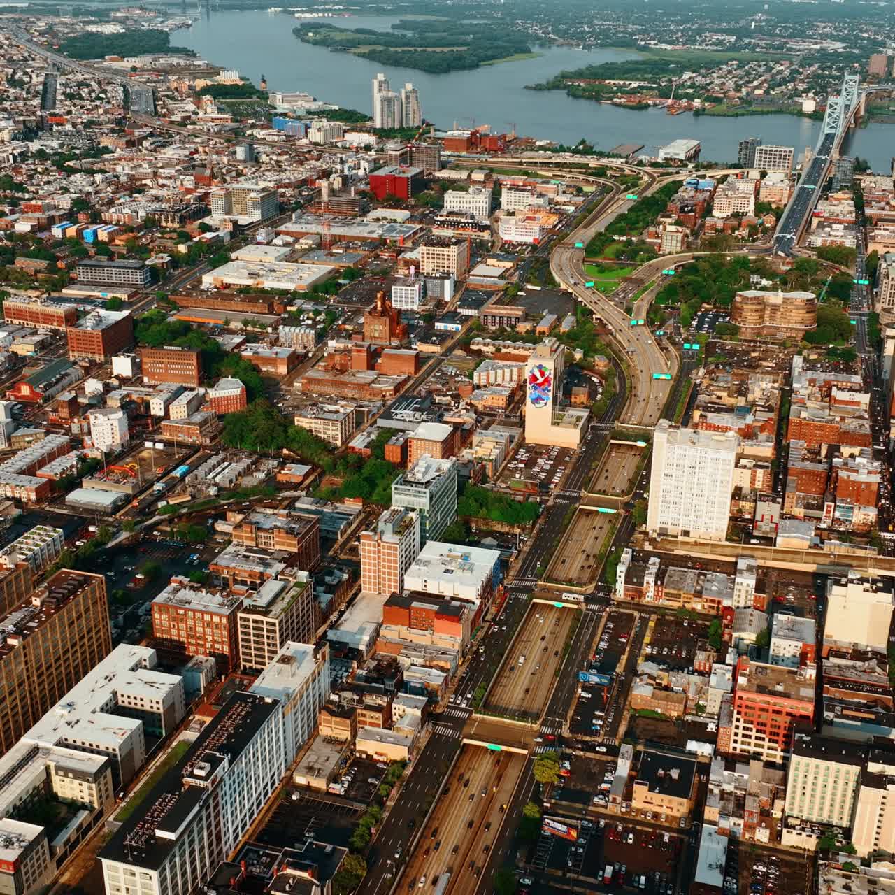 Lively traffic on the roads of Philadelphia at daytime. Vast cityscape with river and bridge at backdrop from top view