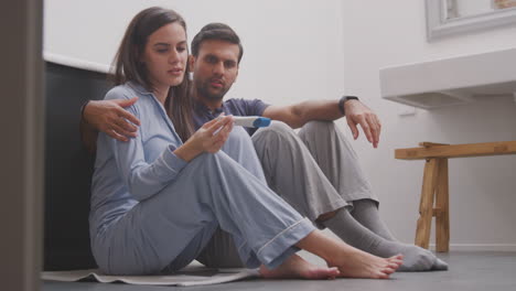 disappointed couple sitting on floor in bathroom at home with negative home pregnancy test