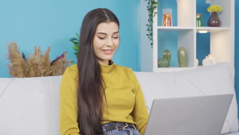 Mujer-Joven-Sonriente-Sentada-En-Un-Sofá-Usando-Una-Computadora-Portátil-Mirando-Un-Mensaje-Escribiendo-En-La-Pantalla,-Trabajando-En-Línea.