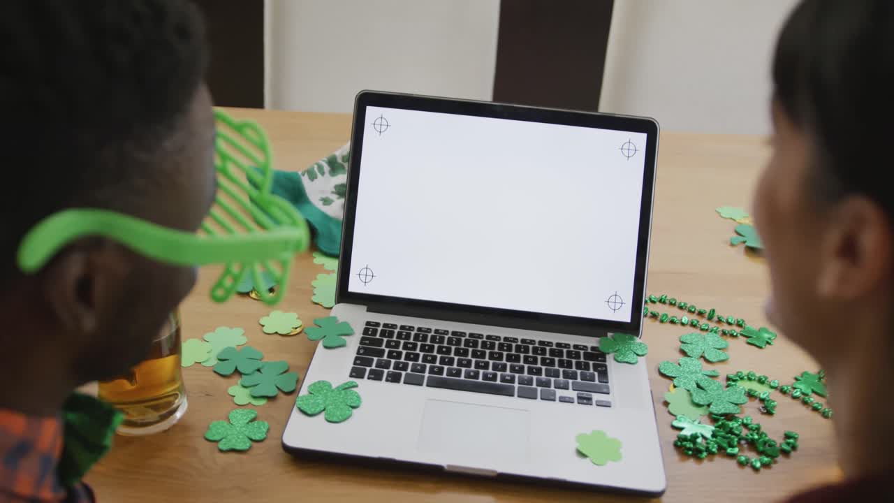 pareja diversa con cerveza vistiendo artículos en forma de trébol y haciendo una videollamada en una computadora portátil con espacio de copia