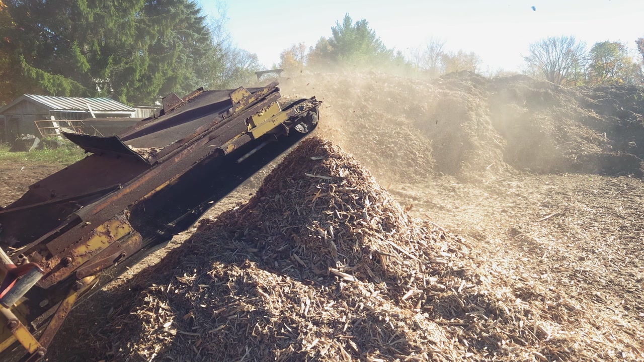 Slow motion wide shot of a wood grinder tossing chips into a piling heap