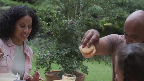 Felices-Padres-Birraciales,-Hijo-E-Hija-Disfrutando-De-La-Comida-En-La-Mesa-Del-Jardín,-Cámara-Lenta