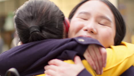 close up of two smiling young female friends meeting and hugging in urban setting together