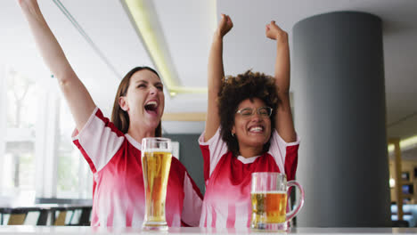 un grupo diverso de amigos felices viendo un juego bebiendo cervezas y abrazándose en un bar