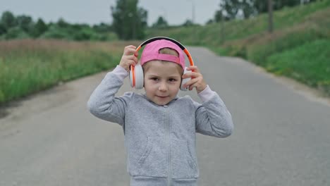 child in cap wearing white headphones to listen to music. leisure time outdoors