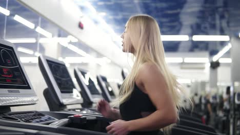 Young-attractive-caucasian-woman-with-blond-hair-in-black-sport-outfit-running-on-treadmil-at-the-gym-in-slomo
