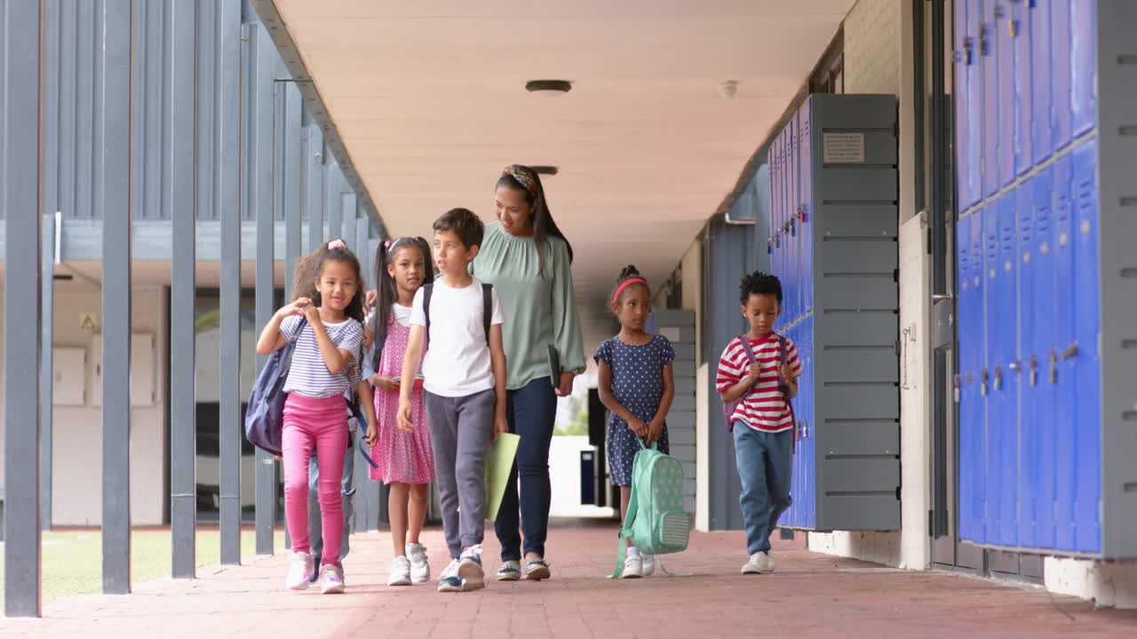 Walking in school hallway, teacher and diverse group of students with backpacks