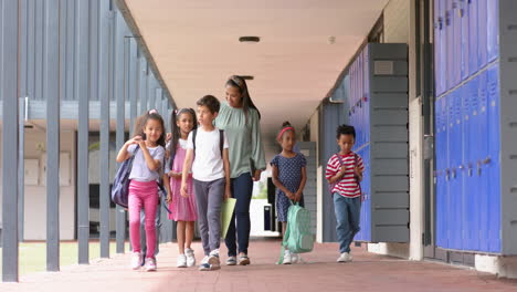 walking in school hallway, teacher and diverse group of students with backpacks