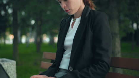 remote worker seated in calm park on wooden bench focused on laptop with lush greenery and trees in background creating peaceful natural workspace