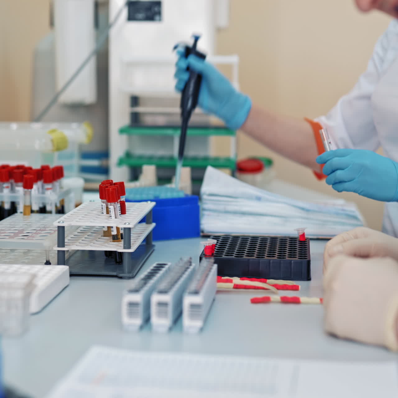 Medical specialists in sterile gloves are working with blood samples on a table in clinic. Senior female nurse teaching young worker to make experiments with blood in the laboratory.
