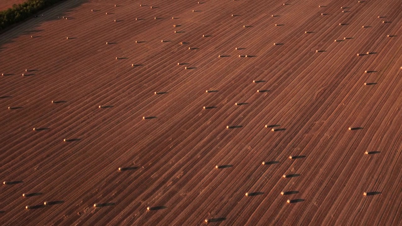 Aerial view showing a farm field with hay bales and distinct plowed lines at sunset