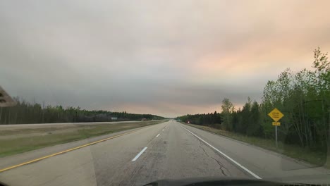 dashcam driving alone along a rural road at sunset, pink orange pastel clouds, end of day, scenic drive, nobody on the freeway, empty, solitude