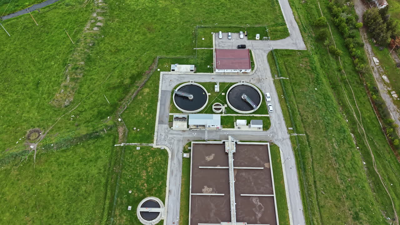 Wastewater treatment facility with multiple tanks and processing areas located in a green landscape during the daytime