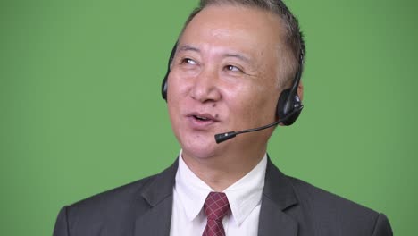 초록색 배경에 콜 센터 대리인으로 일하는 성숙한 일본인 사업가