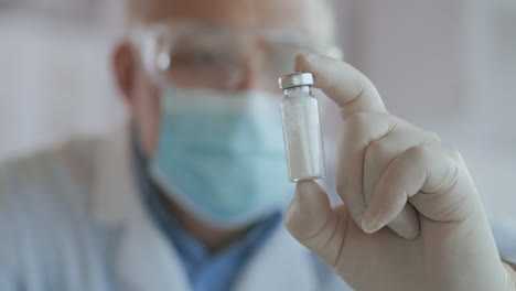 un científico enmascarado que desarrolló una vacuna contra el coronavirus sostiene una ampolla de polvo blanco y examina la vacuna. el médico mira los antibióticos antes de su uso.