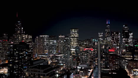 Vista-Aérea-Hacia-Atrás-Sobre-El-Paisaje-Urbano-Iluminado-Por-La-Noche-Del-Río-Norte,-Chicago,-Estados-Unidos