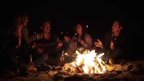 cheerful african american playing guitar for his friends by the fire. multiracial group of young boys and girls sitting by the