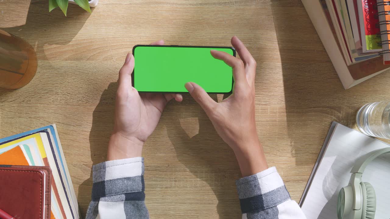 초록색 화면을 모방한 노트북 컴퓨터의 상단에서 아래로 볼 때, 펜, 안경, 그리고 물 한 잔을 가진 노트북 에 나무 사무실 책상 위에 크로마키 디스플레이가 있습니다.