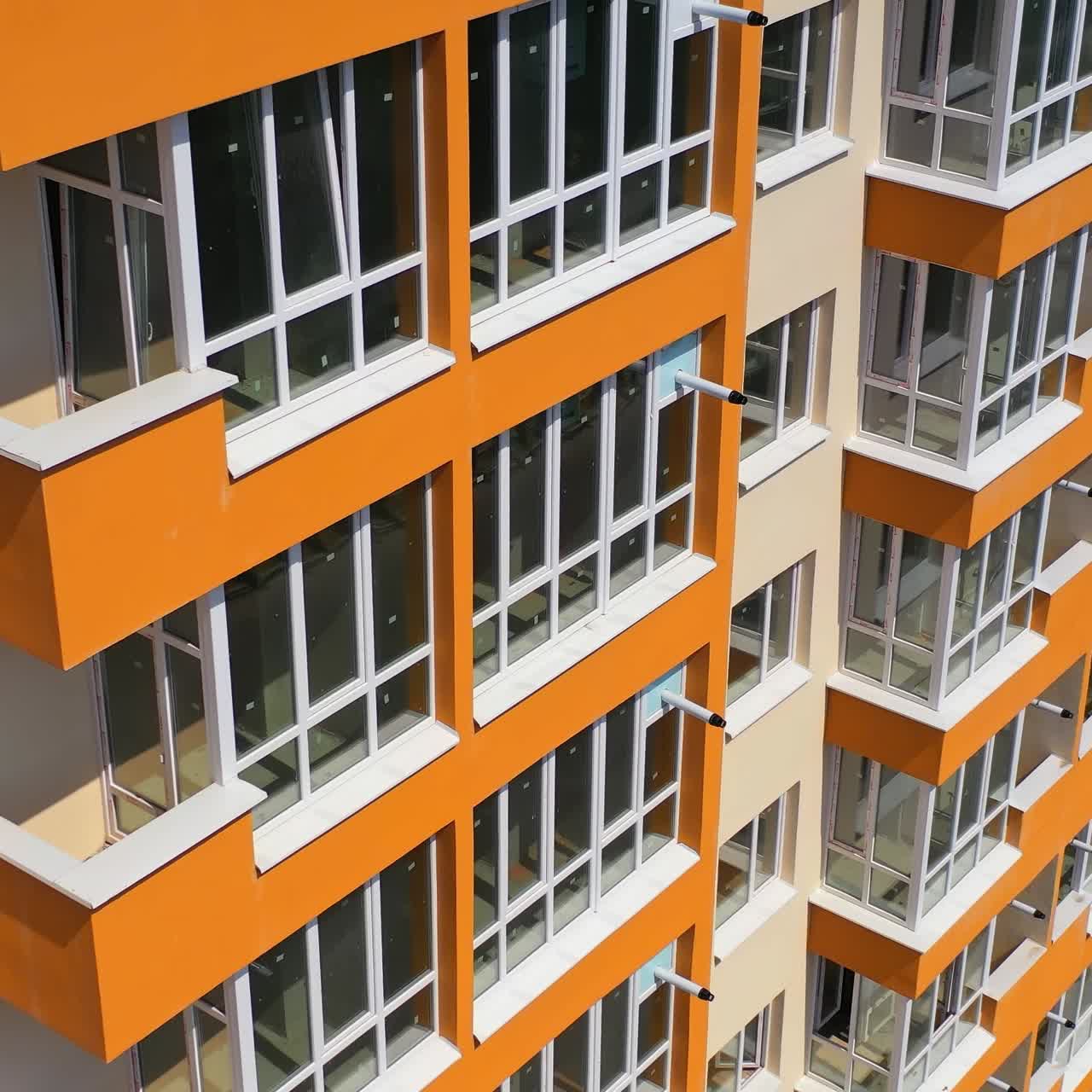 New urban multi storey building. Grey roof and bright orange walls with large balconies of a modern apartment building. Motion camera top down