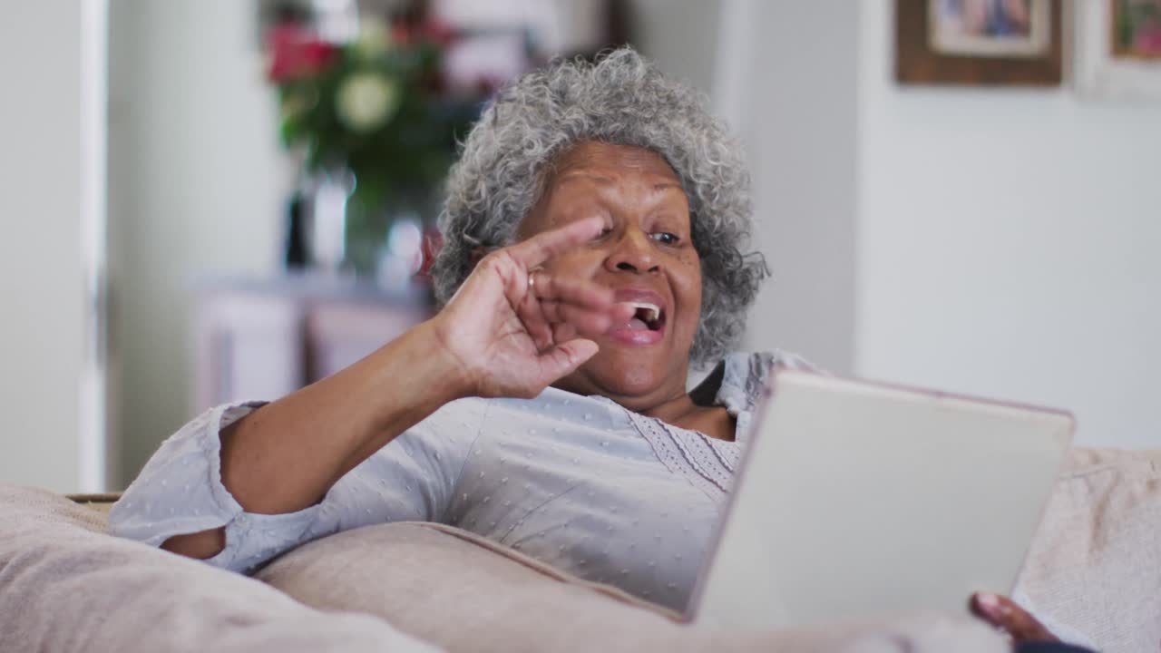 Senior african american woman waving and blowing kisses while having a video call on digital tablet