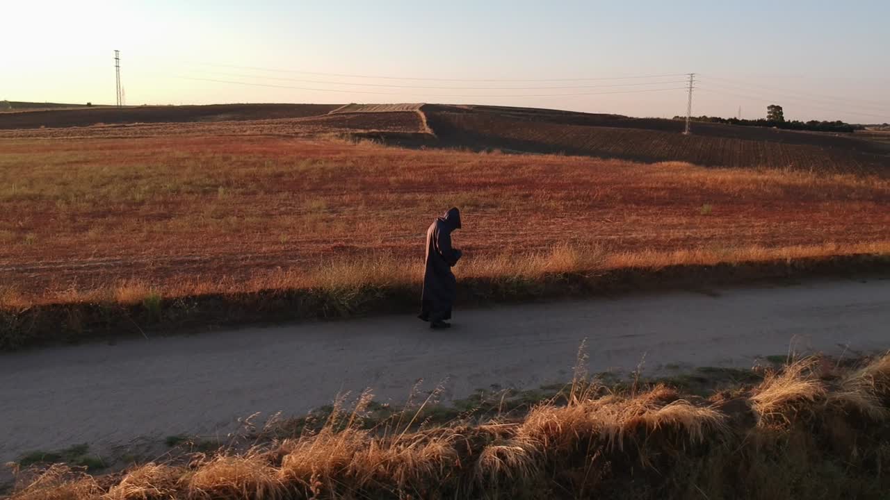A shot from low height following sideways a monk walking on a dirt road
