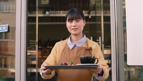 커피숍 밖에 서서 음식 쟁반을 들고 카메라를 보고 웃는 웨이트리스