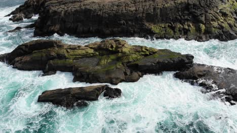 Drone-looks-down-over-sea-rocks-as-waves-crash-into-it