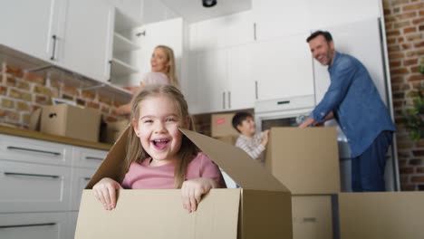 playful girl jumps out of cardboard while moving house