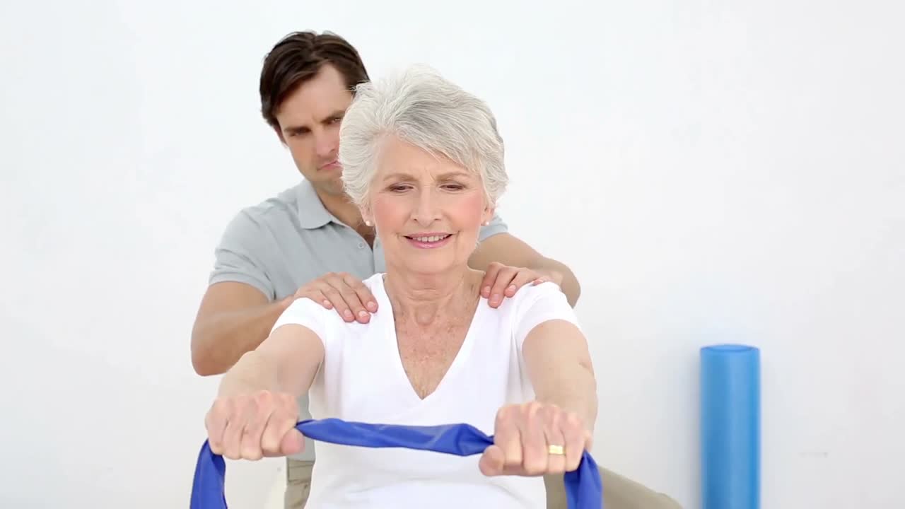 fisioterapeuta comprobando la alineación del hombro de los pacientes de edad avanzada con la banda de resistencia