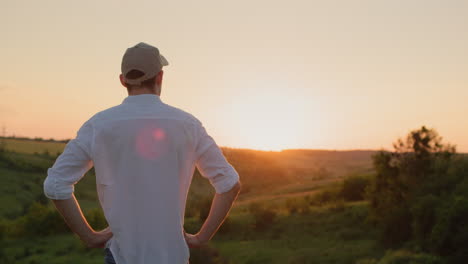 el guapo joven granjero se encuentra frente a un pintoresco paisaje rural mientras el sol se pone.